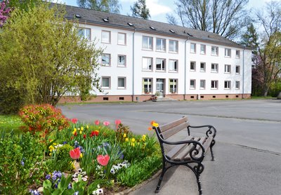 © Geist und Sendung e.V. Haus Benedikt am zentralen Parkplatz, im Vordergrund Blumen und eine Bank